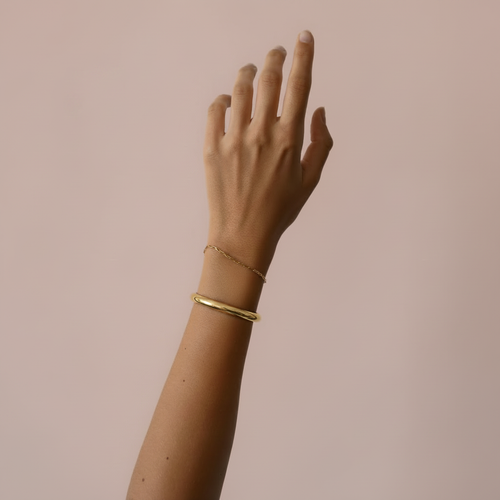 Arm met gouden armband – lichtroze achtergrond